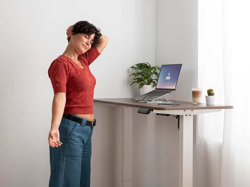 Frau arbeitet am höhenverstellbaren Schreibtisch im Home-Office